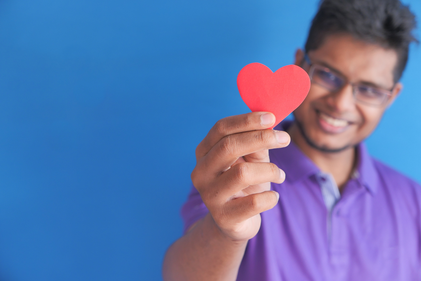 Young Happy Man Holding Red Heart on Blue Background